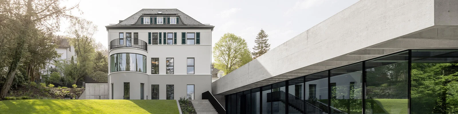 Blick auf eine alte, weiße Villa im Grünen mit modernem Anbau.