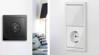 Bildmontage. Links eine schwarze Steckdose an der Wand montiert. Dahinter Blick ins Schlafzimmer. Rechts eine Steckdosen/Schalterkombination übereinander in der Farbe Weiß.