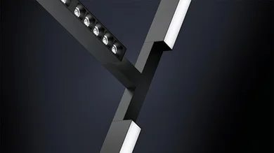 Ein schwarzes, Y-förmiges Leuchtensystem ist vor einem dunklen Hintergrund zu sehen. Die Arme des Systems enthalten sowohl punktuelle als auch flächige Lichtquellen.