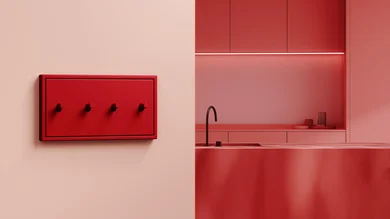 Das Bild zeigt eine moderne, minimalistische Küche in Rottönen. Im Vordergrund befindet sich ein rotes Bedienfeld mit vier Drehknöpfen an der Wand, im Hintergrund eine Küchenzeile mit Spüle und dezentem Licht.