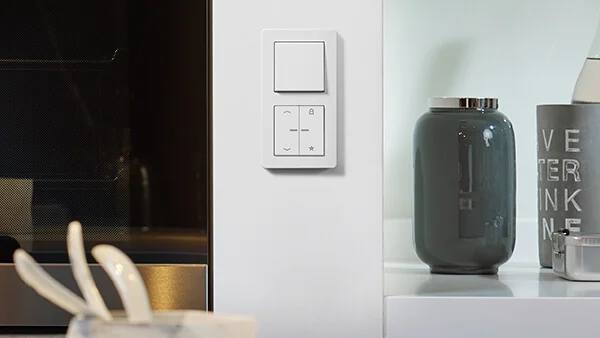 Schalter des Herstellers Jung in der Farbe Weiß an der Wand montiert. Rechts daneben ein Sideboard mit einer Vase in der Farbe Grün.