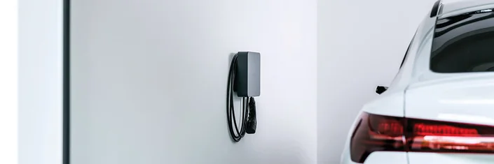 Das Bild zeigt ein weißes Auto von hinten und nebenan eine Wallbox an der Wand.