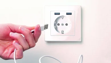 Person hält ein USB-Kabel in der Hand und will es in die weiße Steckdose mit USB stecken.