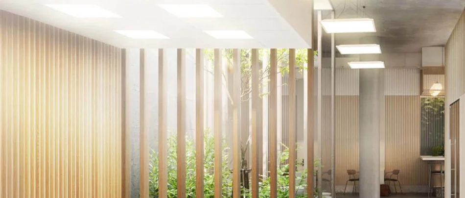 Das Bild zeigt ein modernes, lichtdurchflutetes Büro mit großen Glasflächen, Holzlamellen und viel Grün. Quadratische, flache Deckenleuchten sorgen für eine gleichmäßige und angenehme Beleuchtung im Raum.