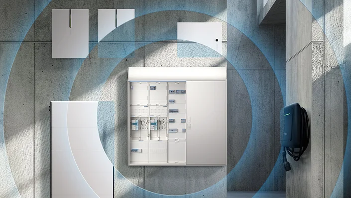 Das Bild zeigt eine moderne Elektroinstallation mit Verteilerkasten, Energiespeicher, Wallbox für E-Mobilität und weiteren Komponenten an einer Betonwand. Blaue Kreise symbolisieren die intelligente Vernetzung der Systeme.