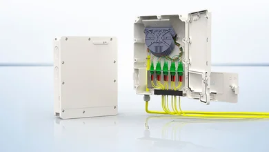 Verteilerkasten einmal geschlossen, einmal geöffnet. Der geöffnete Kasten zeigt das Innere mit grünen Steckern und gelben Kabeln, die nach außen führen.