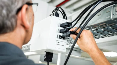 Das Bild zeigt einen Techniker, der an einem weißen Installationsgehäuse unter der Decke mehrere Steckverbindungen an der Kabelrinne anschließt.