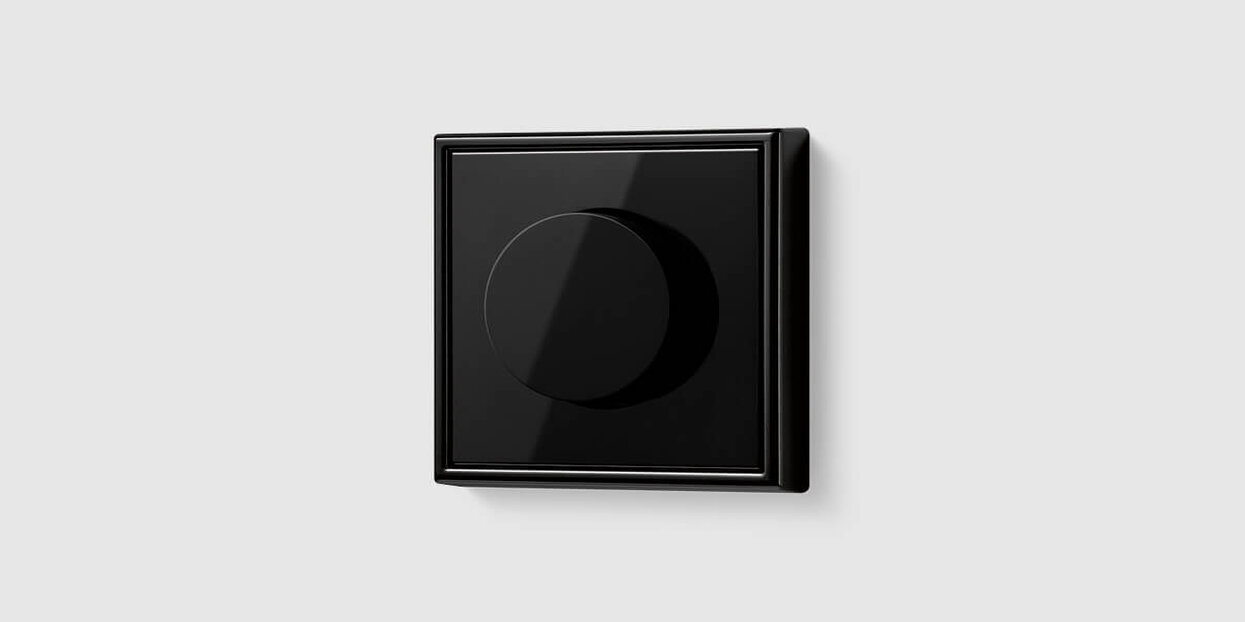 Schwarzer Drehdimmer mit glänzender Oberfläche auf hellem Hintergrund. Das quadratische Bedienelement verfügt über einen mittig angeordneten Drehknopf. Geben Sie Ihr Feedback zu BizChat ab.