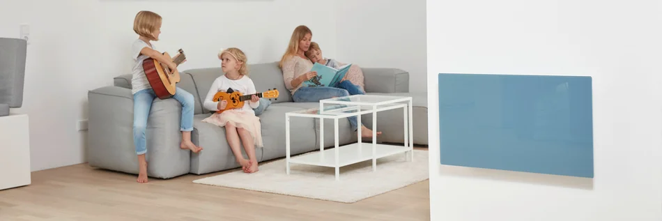 Eine Person sitzt mit drei Kindern auf einem Sofa. Im Vordergrund ist ein blaues Raumheizgerät an der Wand befestigt.