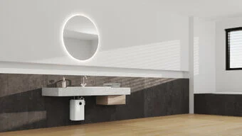 Das Bild zeigt ein modernes und stilvolles Badezimmer, in weißen, hellen Farben mit großem runden Spiegel und einem STIEBEL ELTRON Kleinspeicher SNU 5 Plus unter dem Waschbecken..