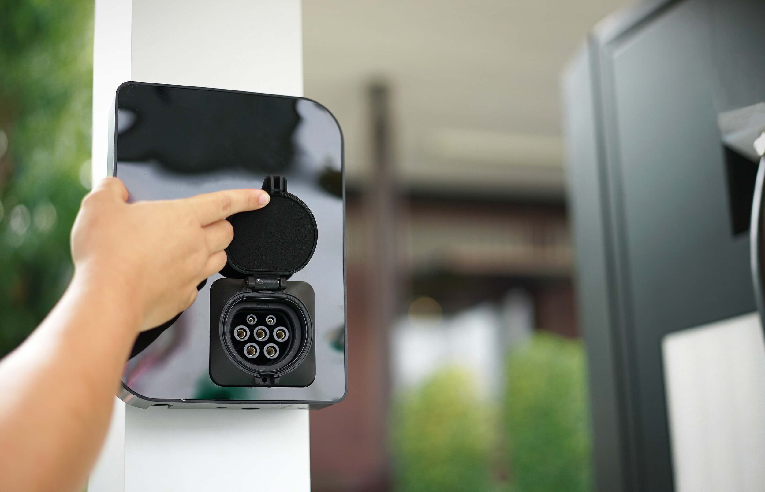 Eine Person bedient eine Wallbox mit der Hand.
