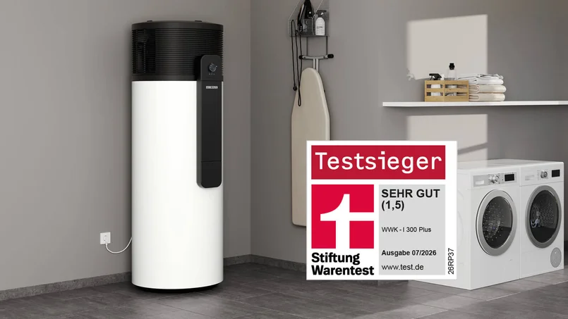 Warmwasser-Wärmepumpe im Hauswirtschaftsraum neben Waschmaschinen und Haushaltszubehör. Hervorgehoben wird die Auszeichnung als Testsieger der Stiftung Warentest mit dem Urteil „Sehr gut (1,5)”