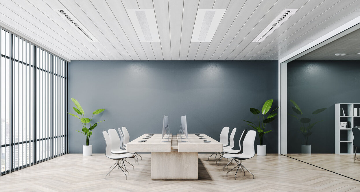 Ein modernes, helles Büro mit großem Tisch, mehreren Stühlen, Monitoren und großen Fensterfronten sowie Pflanzen an den Seiten.