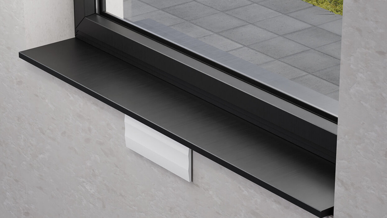 Auf dem Bild ist ein Fenster mit schwarzer Fensterbank zu sehen, unter der ein weißes rechteckiges Lüftungselement an der Wand montiert ist.