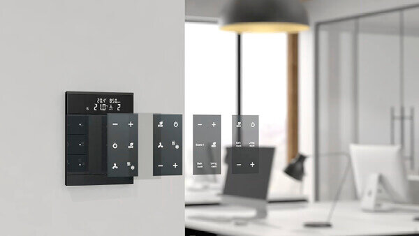 Das Bild zeigt ein schwarzes Busch-Tenton® Bedienelement auf einer weißen Wand. Grafisch wurden dabei 4 verschiedene Bedieneroberflächen im Bild nebeneinander angeordnet. Im Hintergrund stehen ein Schreibtisch mit weißem Bildschirm und weiße Lampe.