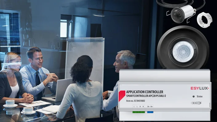 Das Bild zeigt ein Meeting in einem modernen Konferenzraum. Im Vordergrund sind Komponenten eines intelligenten Lichtsteuerungssystems zu sehen: ein Application Controller der Serie SMARTCONTROLLER sowie zwei verschiedene Präsenzmelder..
