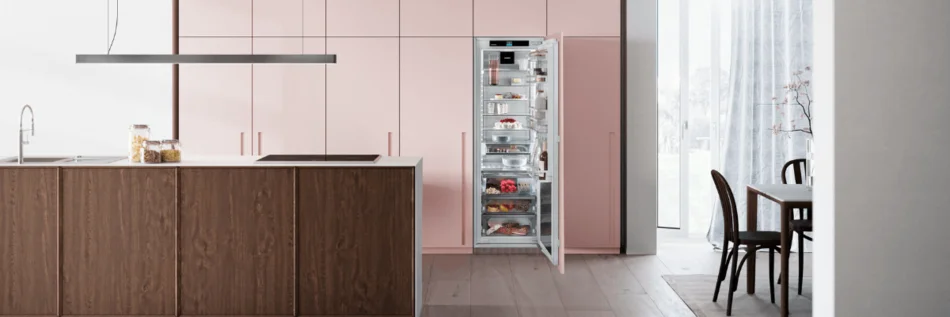 Helle Wohnküche im Hintergrund Küchenfront in der Farbe Rosa mit einem geöffneten Einbaukühlschrank von Liebherr.