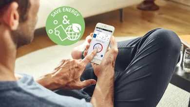 Auf diesem Bild ist eine Person auf einem Sofa sitzend von hinten zu sehen, die gerade mit dem Smartphone etwas steuert.