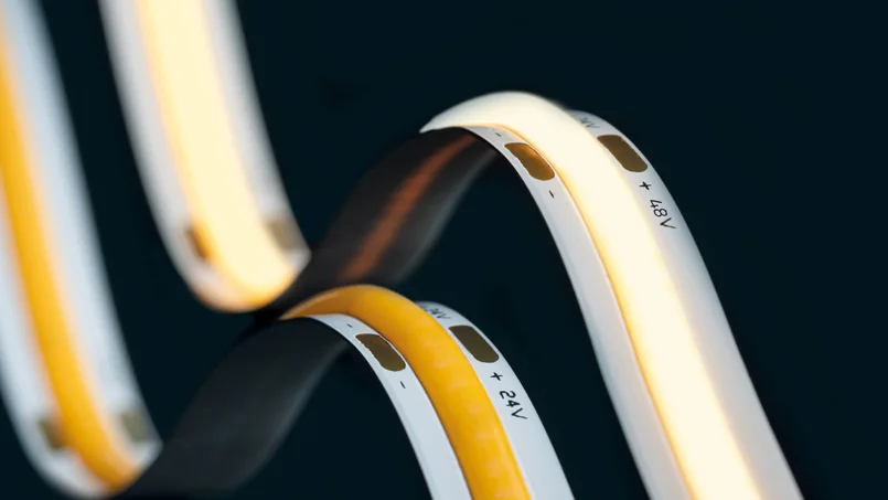 Zu sehen ist eine Nahaufnahme von beleuchteten LED-Streifen in warmweiß und gelb. Die gebogenen Elemente sind vor dunklem Hintergrund stark in Szene gesetzt.