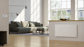 Das Bild zeigt ein Wohnzimmer mit Sofa. Im Vordergrund ist eine Natursteinheizung an einer halbhohen Wand befestigt 