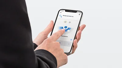 Person hält ein Smartphone in der Hand und bedient das Display. Aufnahme von leicht schräg hinten.