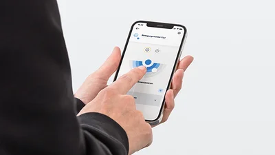 Person hält ein Smartphone in der Hand und bedient das Display. Aufnahme von leicht schräg hinten.