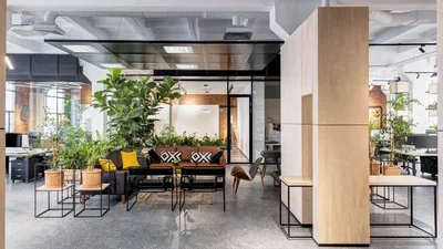 Ein modernes Büro mit Lounge-Bereich, Sofas und Sesseln, umgeben von vielen Pflanzen und großen Fenstern.