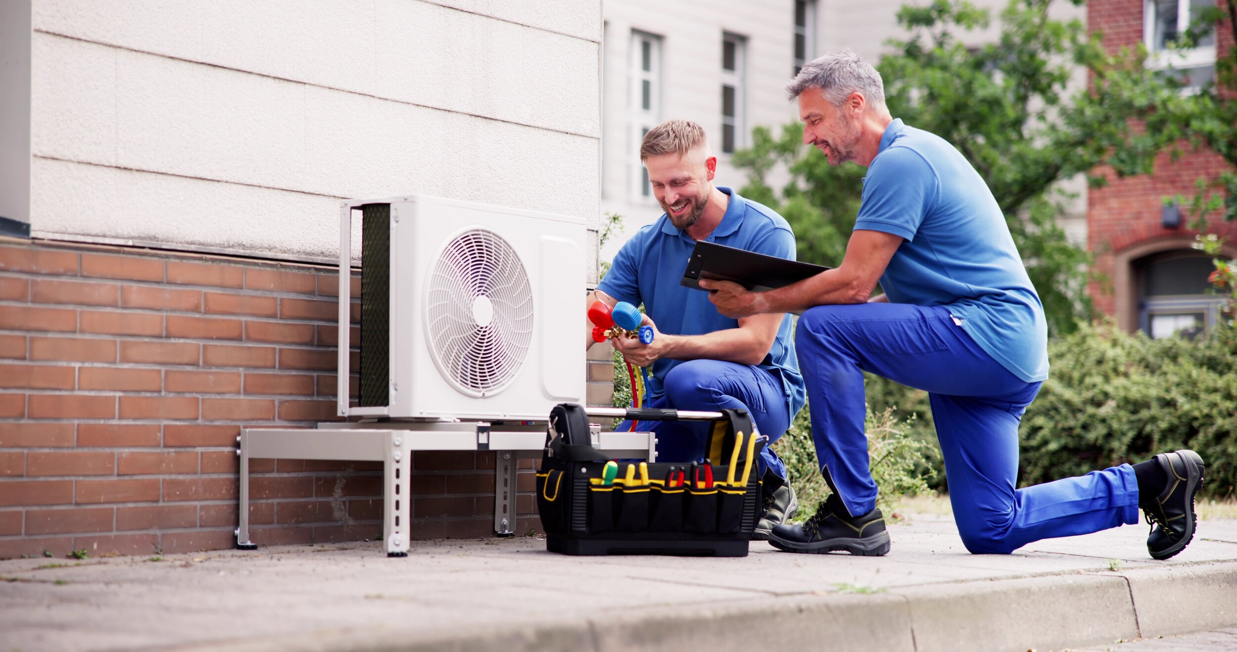 Das Bild zeigt zwei Handwerker, die gerade draußen eine Wärmepumpe anbauen.