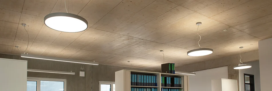 Über einem weißen Regal mit Aktenordnern sind an der Decke große runde Leuchten angebracht.