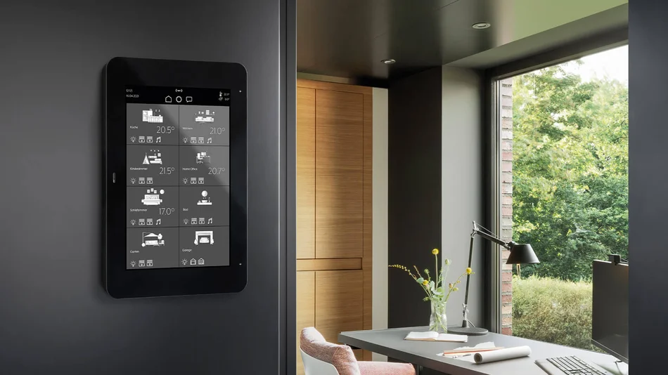 Zu sehen ist ein schwarzes KNX-Smart-Panel an der Wand in einem modern eingerichteten Raum. Auf dem Display werden verschiedene Wohnbereiche und Temperaturen angezeigt.