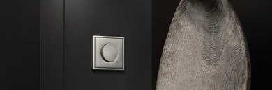 Regler für ein Thermostat in der Farbe Hellgrau an der Wand. Daneben ein Handtuch aufgehängt.