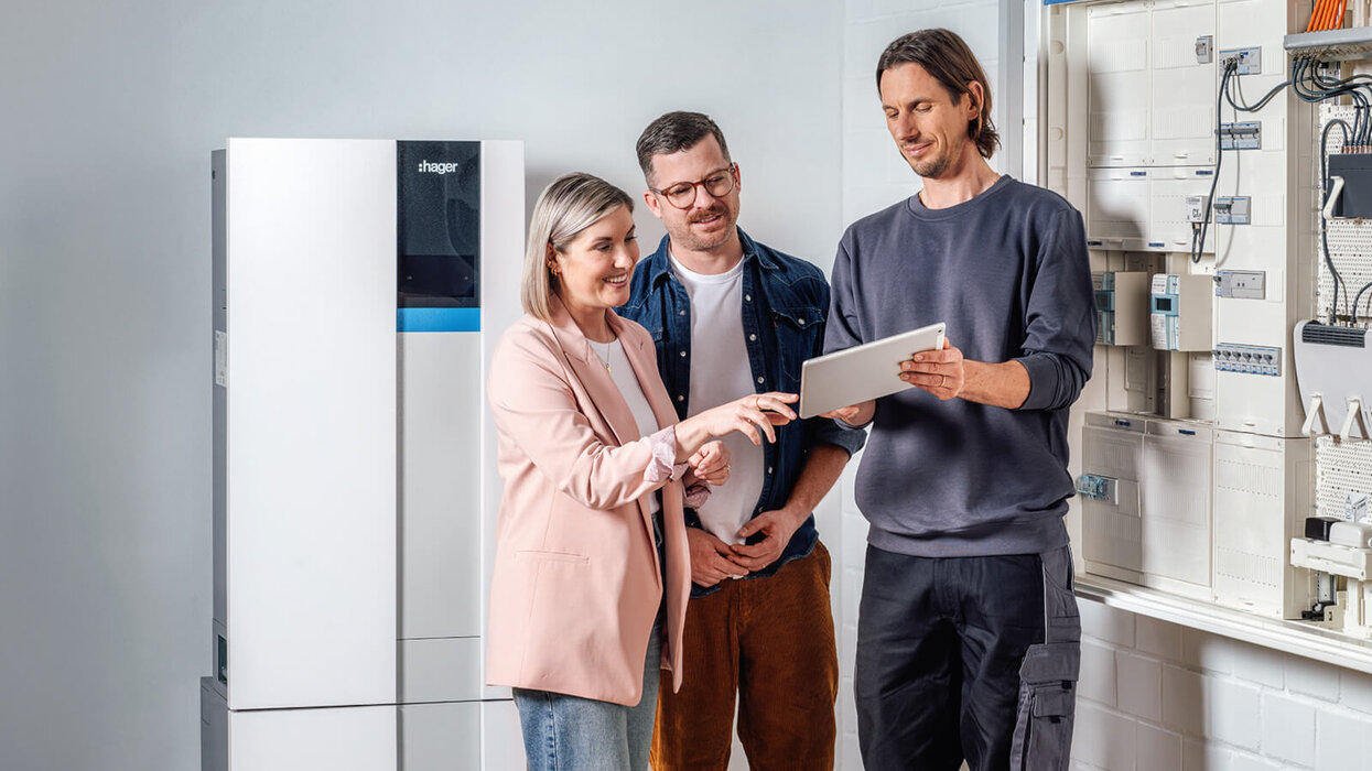 3 Personen. Person ganz rechts erklärt den beiden anderen etwas. Im Hintergrund ist ein Energiespeicher zu sehen.