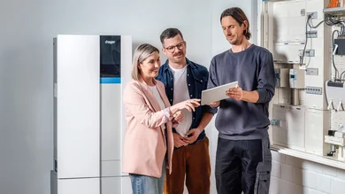 3 Personen. Person ganz rechts erklärt den beiden anderen etwas. Im Hintergrund ist ein Energiespeicher zu sehen.