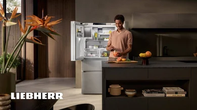 Das Bild zeigt eine moderne Küche, in der eine Person vor einem geöffneten Liebherr-Kühlschrank steht und ein Getränk zubereitet.