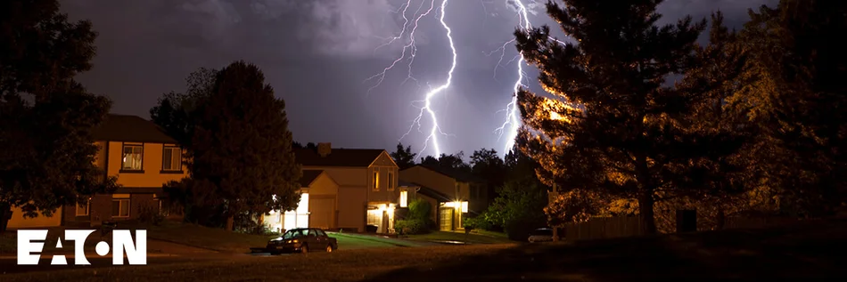 Das Bild zeigt auf der linken Seite eine Reihe von kleinen Wohnhäusern mit Garagen. Gegenüber von der Häuserzeile stehen große Bäume. Der Nachthimmel wird von zwei Blitzen erhellt. In der linken unteren Bild-Ecke ist das Logo des Herstellers Eaton abgebildet.
