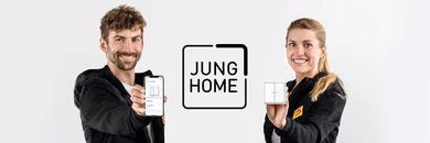 Zwei Personen zugewandt zum Betrachter. Links hält ein Mann ein Smartphone hoch. Rechts eine Frau, die einen Schalter in der Hand hat. In der Mitte das Logo vom Hersteller Jung Home.