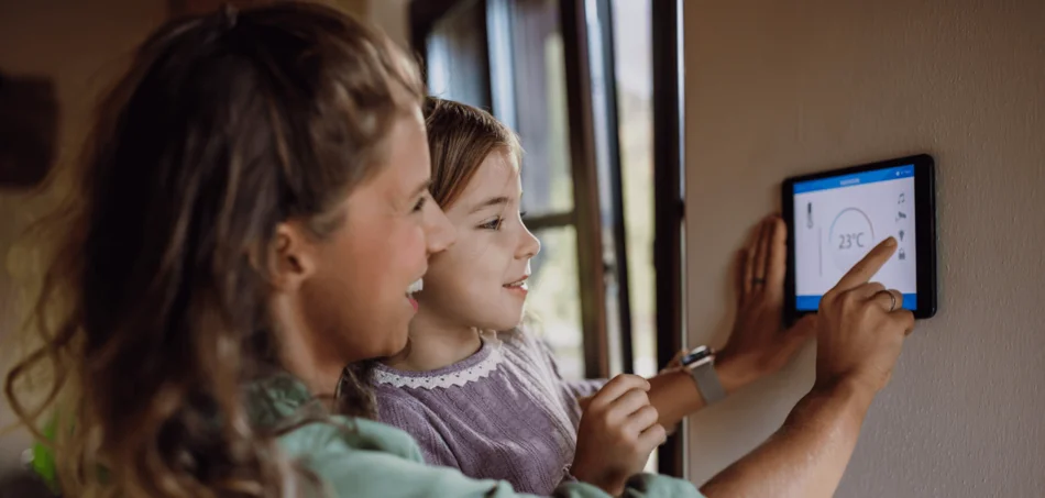Frau mit Kind stehen vor einem Display, welches an der Wand montiert ist. Sie bedienen den Touchscreen gemeinsam.