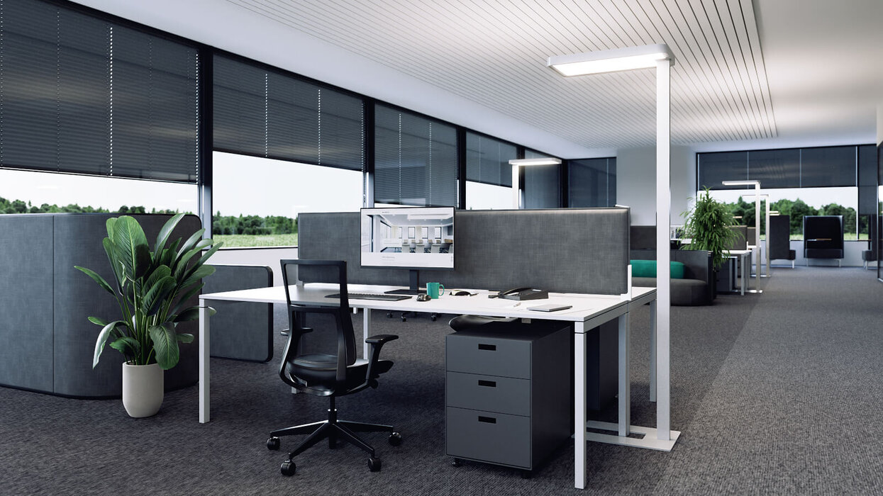 Das Bild zeigt ein modernes Großraumbüro mit großzügiger Fensterfront, ergonomischem Arbeitsplatz und schlanken LED-Stehleuchten neben den Schreibtischen.