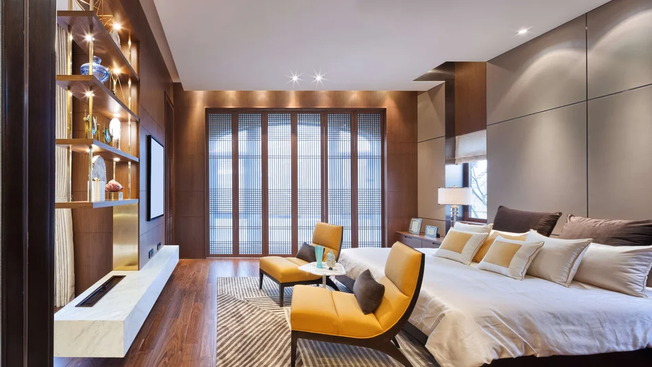 Bild zeigt ein Schlafzimmer im edlen Ambiente mit zwei gelben Stühlen vor dem Bett und einer stimmungsvollen Beleuchtung.