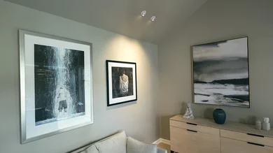 Modern eingerichteter Wohnraum mit drei Kunstwerken an der Wand, hellem Sideboard mit Deko-Elementen und indirekter Beleuchtung.