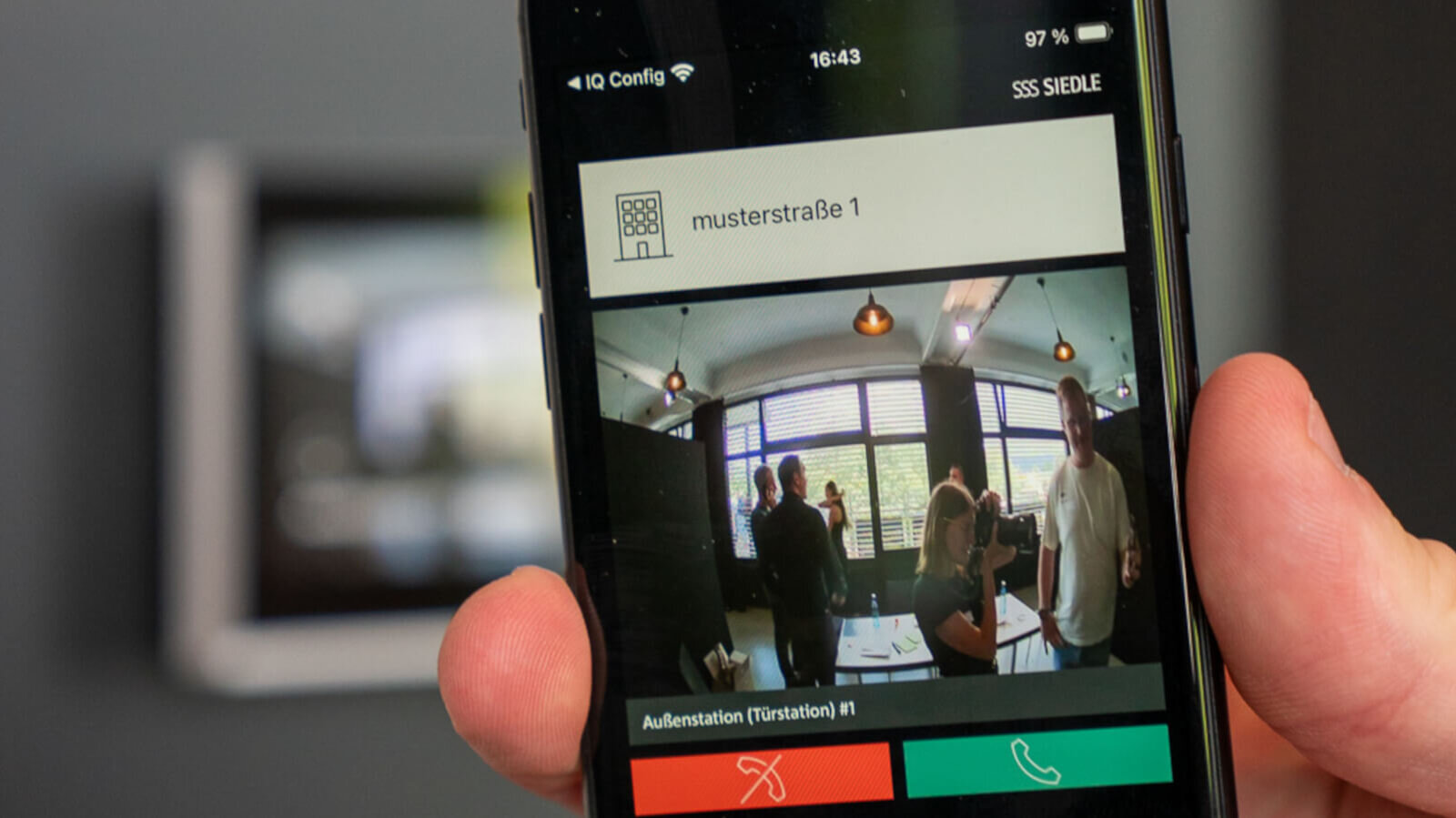 Das Bild zeigt ein Smartphone in der Hand, auf dessen Display die Siedle-App mit Live-Video der Türstation und Annehmen-/Ablehnen-Symbolen eingeblendet ist.