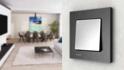 Schalter Delta in der Farbe Schwarz an der Wand und im Hintergrund eine Wohnlandschaft mit Esstisch..