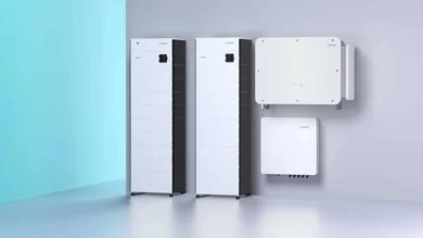 Das Bild zeigt eine moderne Energieanlage mit zwei hohen, schlanken Batteriespeichern und zwei kleineren Wandgeräten, die an einer hellgrauen Wand montiert sind. Im Hintergrund ist eine leuchtend türkise Wand zu sehen, die einen Kontrast zur technischen Ausstattung bildet.
