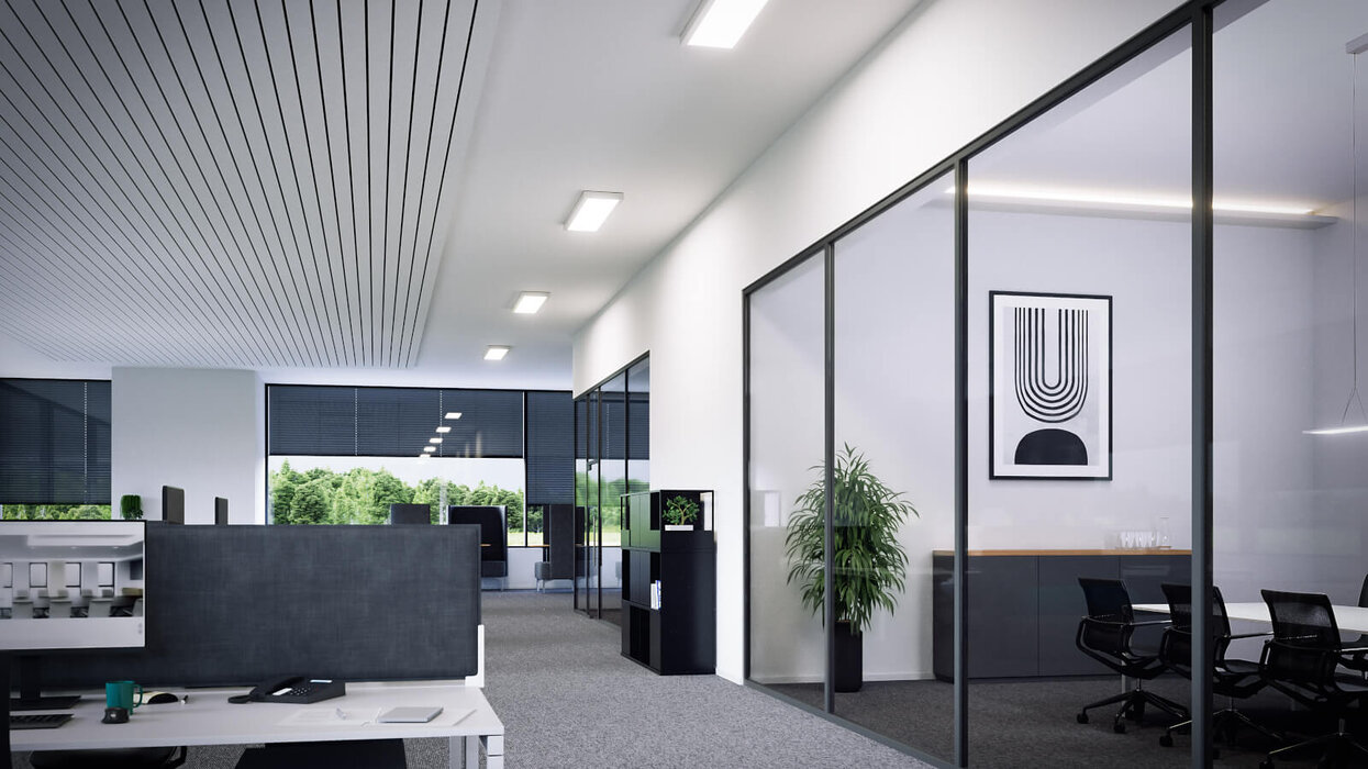 Ein modernes Büro mit offenen Arbeitsplätzen und Glasbesprechungsraum, ausgestattet mit mehreren rechteckigen Deckenleuchten, die gleichmäßig für helle Ausleuchtung sorgen.