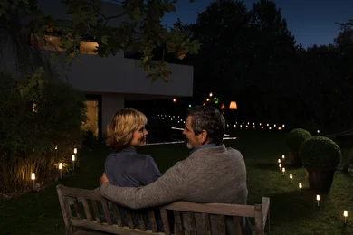 Zwei Personen auf einer Bank im Garten in der Dämmerung, die sich umarmen.