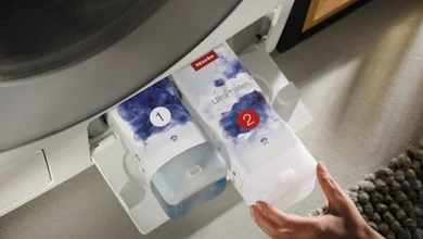 Blick von oben auf das TWIN Dos system von Miele, welches gerade von einer Person in den unteren Bereich der Waschmaschine eingeführt wird.