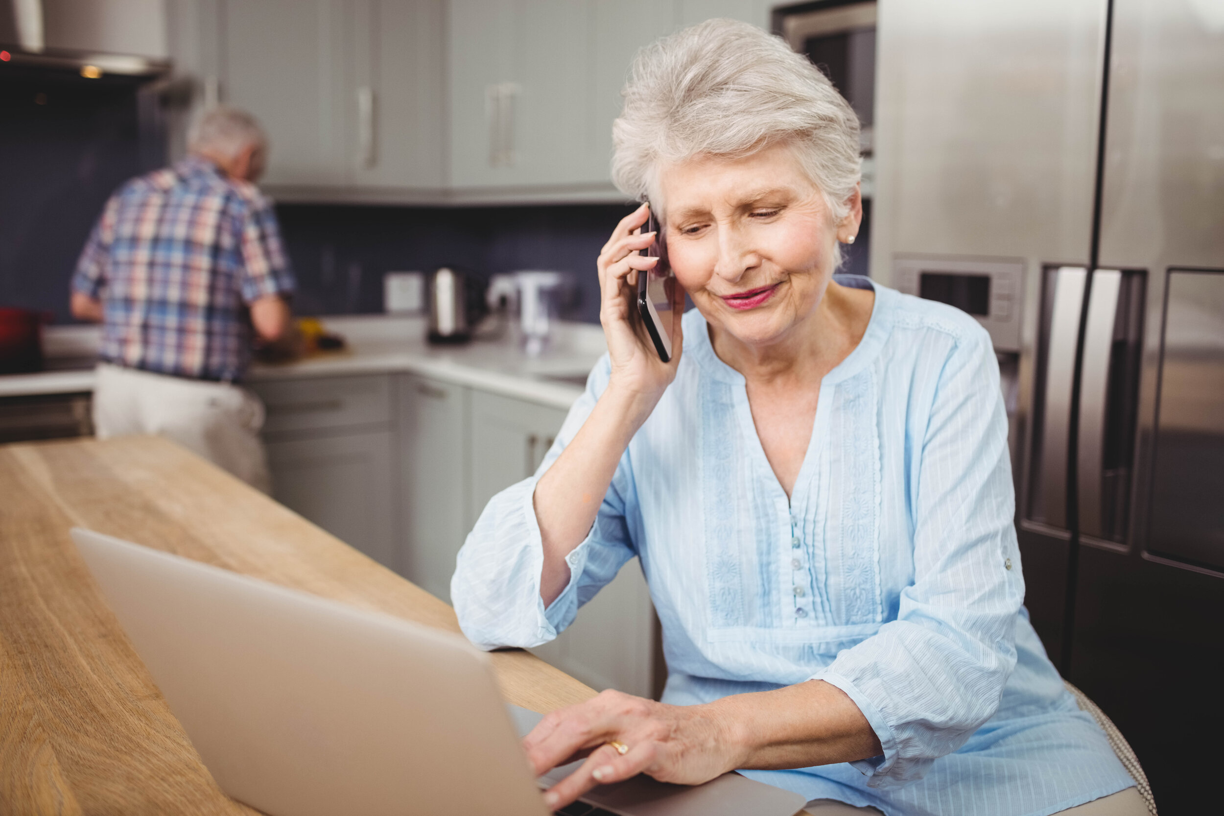 Dieses Bild zeigt eine Seniorin, die am Küchentresen telefoniert.