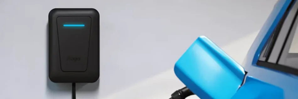 Das Bild zeigt eine schwarze Ladestation an einer weißen Wand. Ein schwarzes Ladekabel führt zu der geöffneten Tankklappe eines metallic-blauen Autos.