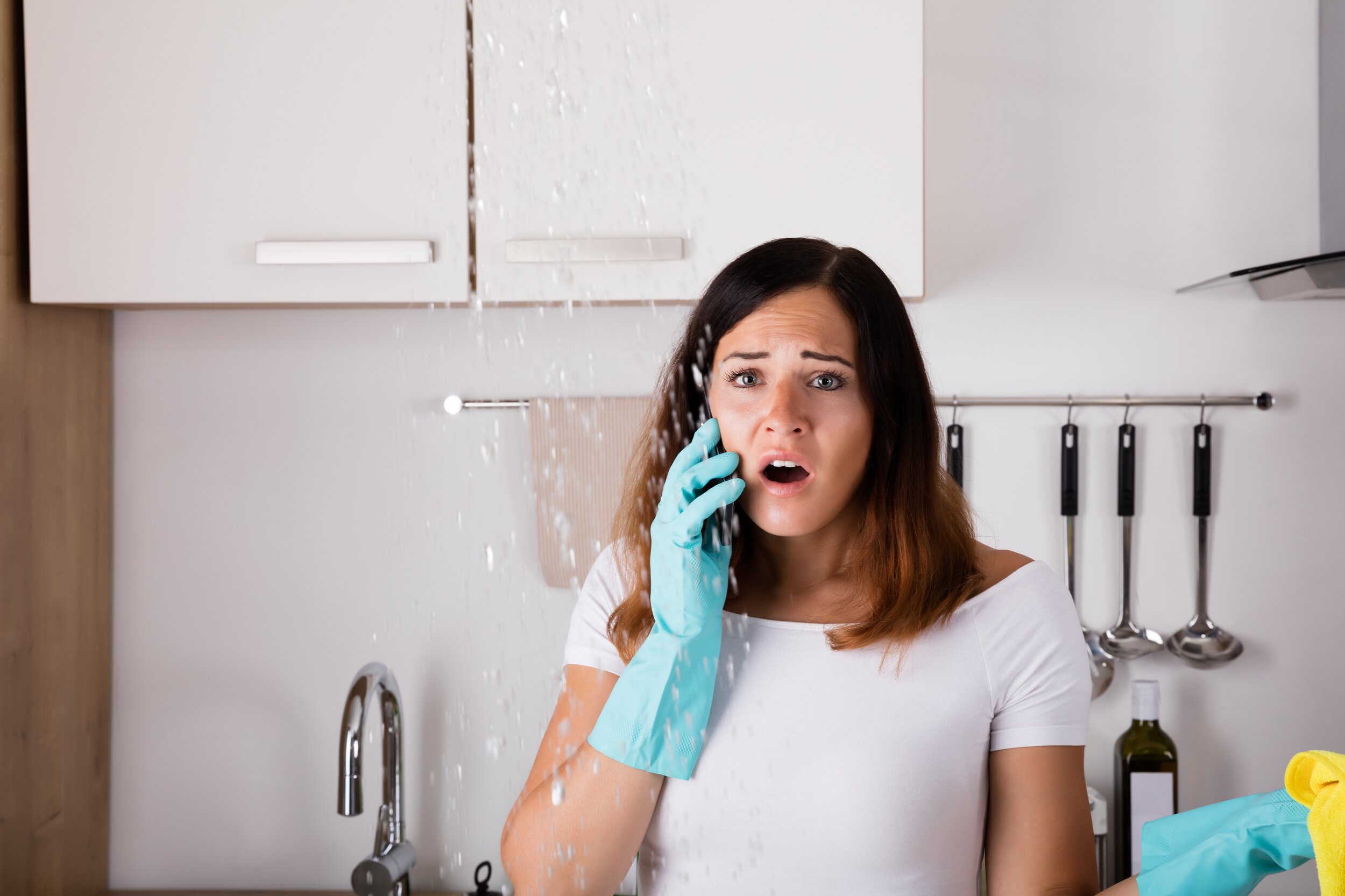 Das Bild zeigt eine erschrockene Frau, die vor einem Wasserschaden steht.