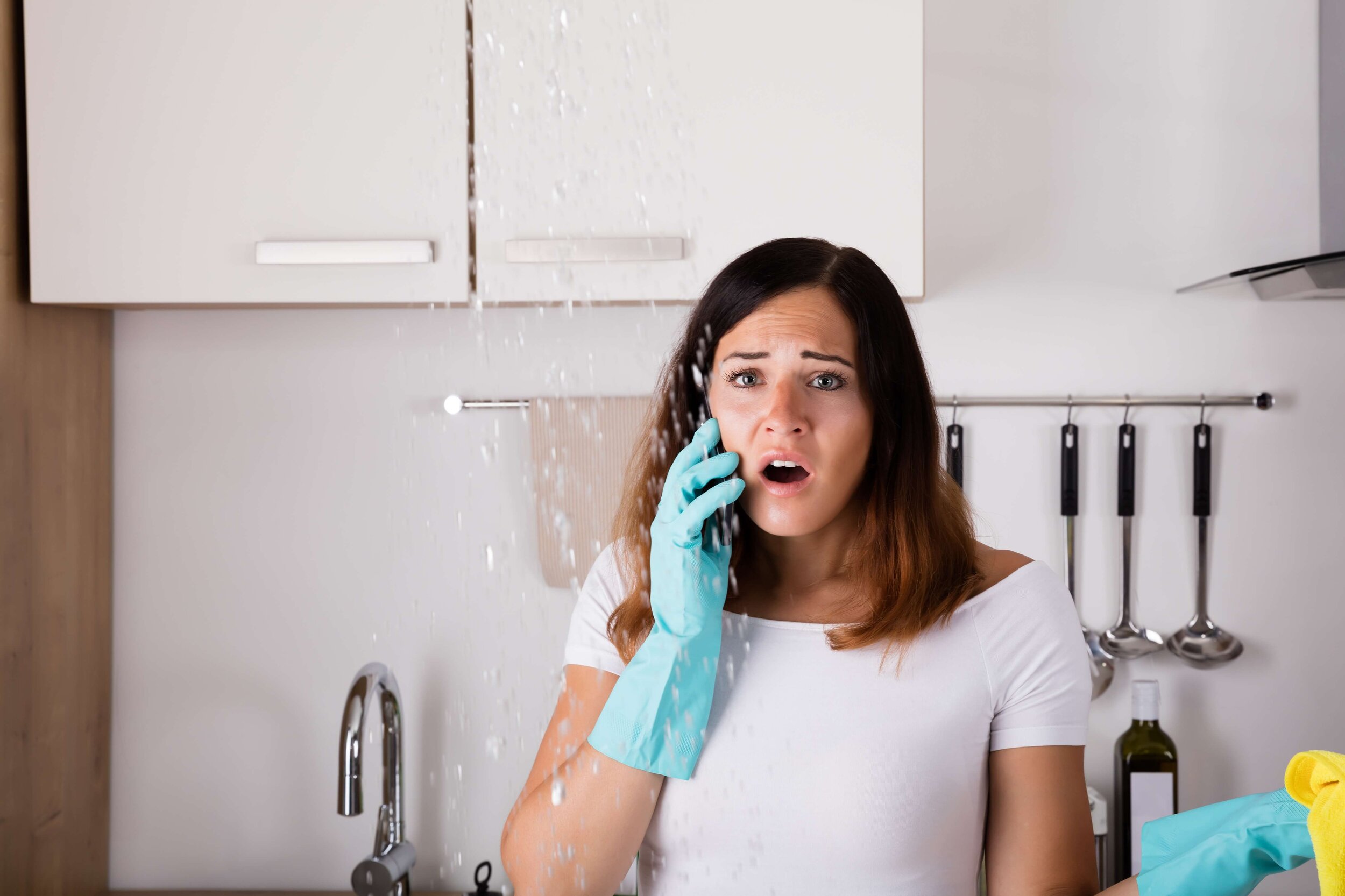 Das Bild zeigt eine erschrockene Frau, die vor einem Wasserschaden steht.